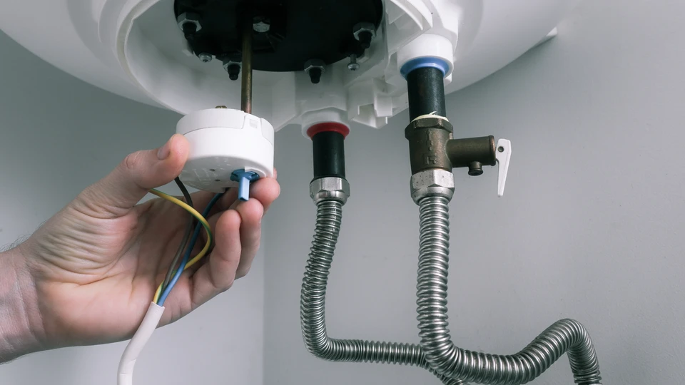 Int&eacute;rieur r&eacute;sidentiel, technicien installant un chauffe-eau &eacute;lectrique au plafond, manipulation des raccordements &eacute;lectriques avec c&acirc;bles apparents