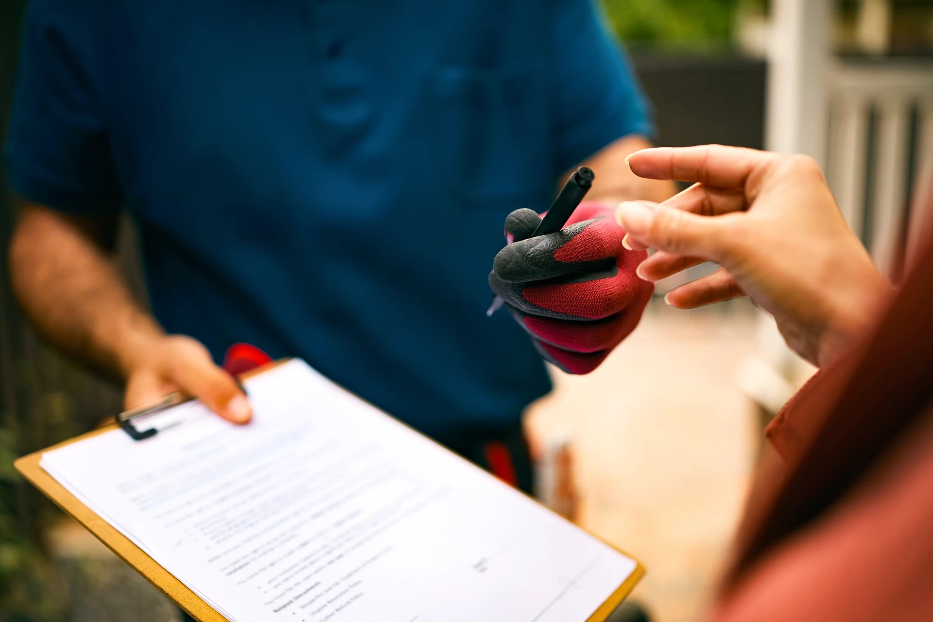 Une personne en costume signe des documents sur un bureau avec un stylo, une petite maison miniature en bois au toit rouge et une tasse de café
