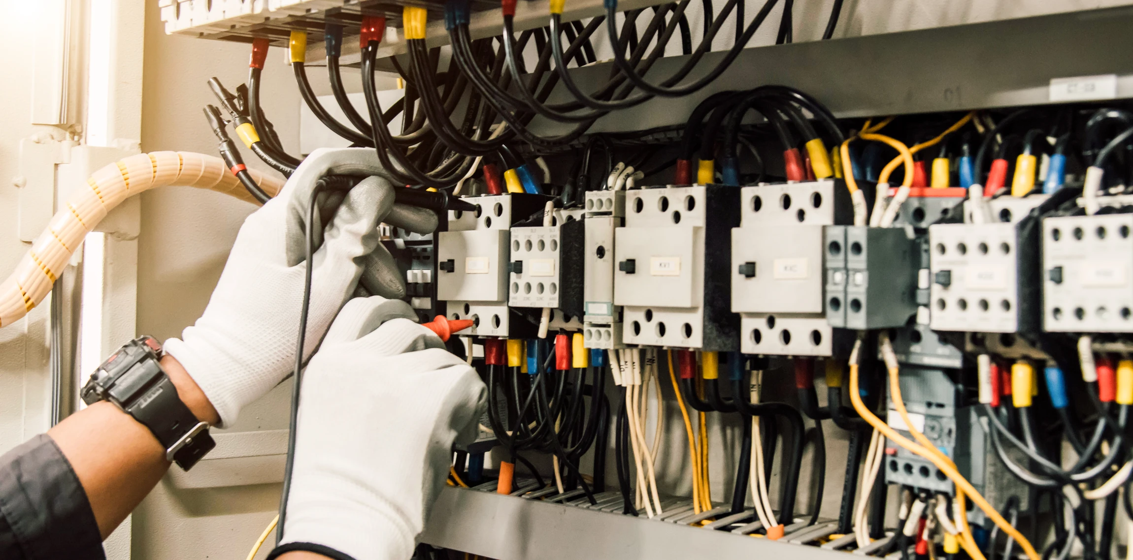 Intérieur de chantier, électricien barbu portant casque blanc et lunettes de sécurité jaunes travaille sur tableau électrique mural