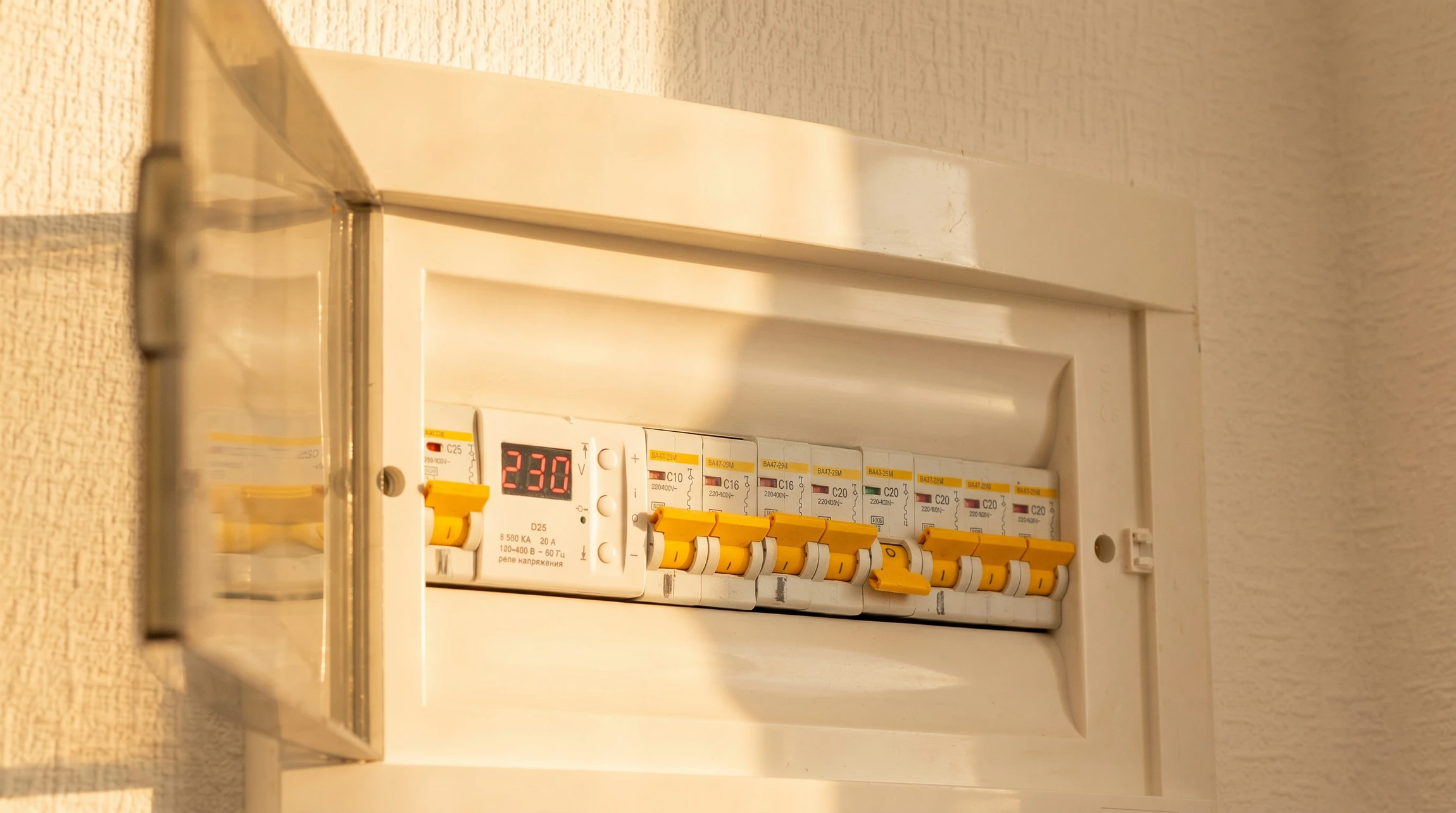Technicien en combinaison bleue effectuant des mesures électriques sur un tableau de contrôle industriel avec un multimètre à pinces ampèremétriques