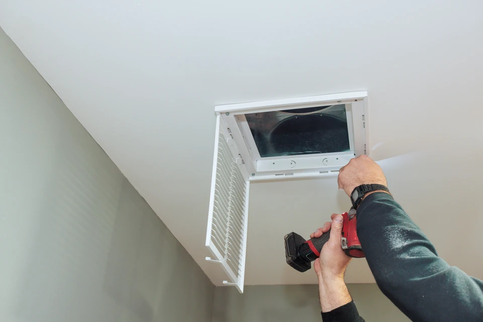 Installation de VMC discrète et soignée dans une cuisine moderne : gaines blanches finement intégrées au plafond suspendu, bouche d'extraction murale avec finitions épurées et nickel, absence de marques ou de désordre, passages de gaines nets et parallèles aux lignes architecturales de la pièce. Plan rapproché montrant la précision d'exécution avec des finitions parfaites et impeccables.