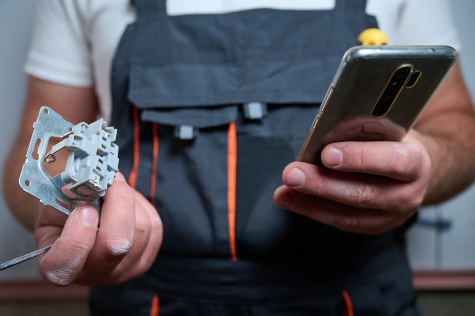 Photographie d'un &eacute;lectricien en uniforme professionnel travaillant &agrave; l'int&eacute;rieur d'un logement r&eacute;sidentiel, effectuant une installation &eacute;lectrique visible (tirage de c&acirc;bles, installation d'appareillage &eacute;lectrique mural, ou travail sur un tableau &eacute;lectrique). Le technicien est concentr&eacute; sur son intervention. L'arri&egrave;re-plan montre un int&eacute;rieur r&eacute;sidentiel moderne et propre. La sc&egrave;ne doit transmettre le professionnalisme, la comp&eacute;tence technique et l'engagement direct de l'artisan sur le chantier.