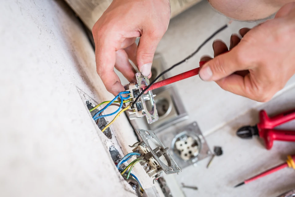 Électricien en combinaison bleue installant une prise électrique murale dans un intérieur résidentiel blanc