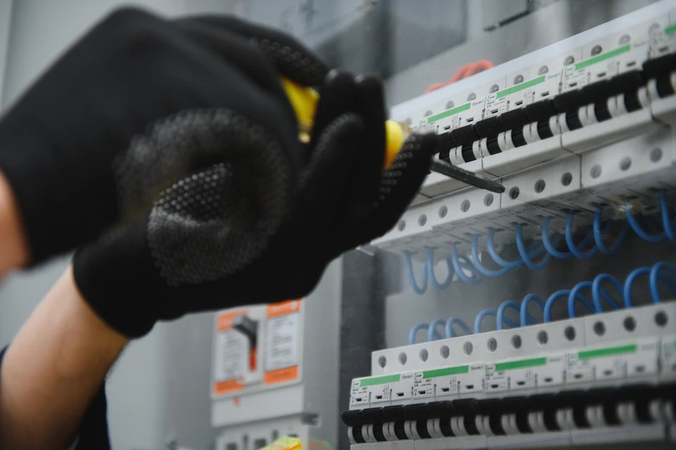 Un électricien travaille sur une installation électrique murale dans un intérieur résidentiel